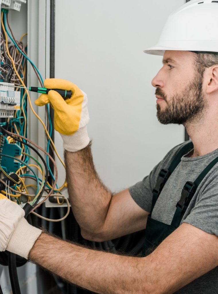 side-view-of-handsome-bearded-electrician-repairing-electrical-box-and-using-screwdriver-in-corridor-rjj9dfwh2ayo87a8k8pj4yiotd36zc50uxmt0r260w